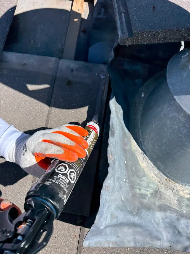 Applying exterior thermoplastic sealant at a chimney flashing junction on a concrete tile roof in Calgary