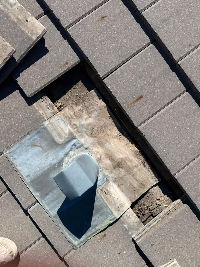 Concrete roof tiles lifted to expose the lead flashing pan around a vent during a leak repair in Calgary