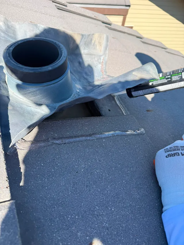 Roofer running a fresh sealant bead along a plumbing vent flashing on a concrete tile roof in Calgary